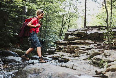 Woman with backpack hiking in mountains, spending vacations. woman crossing the mountain stream