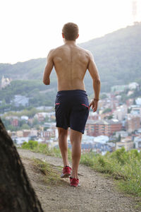 Rear view of physically challenged shirtless man jogging against cityscape