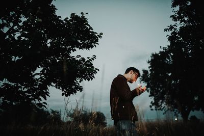 Side view of smoking cigarette while standing on field against sky