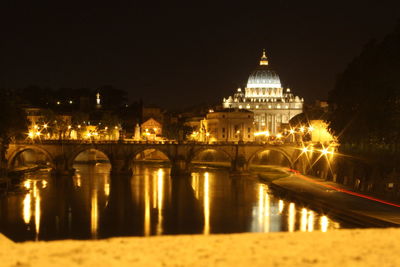 Illuminated st peter basilica by bridge over river at night