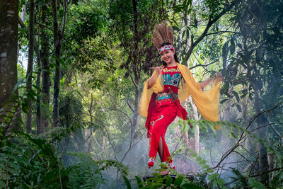 Portrait of young woman performing dance by trees in forest