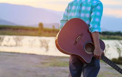 Midsection of man carrying guitar at lakeshore