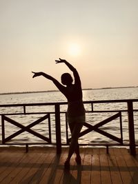 Silhouette woman dancing on pier over sea against clear sky