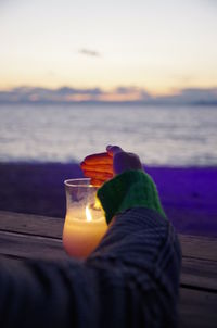 Low section of woman standing by sea against sky during sunset