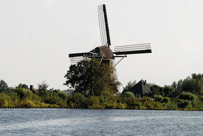 Traditional windmill by lake against sky