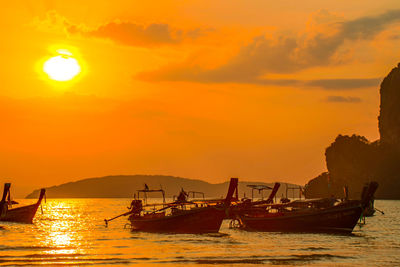 Silhouette fishing boats in sea against orange sky