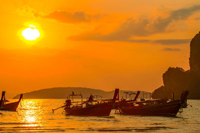 Silhouette fishing boats in sea against orange sky