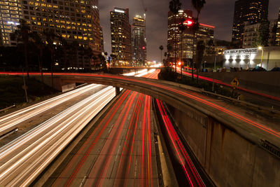 Light trails on bridge over road by illuminated buildings at night