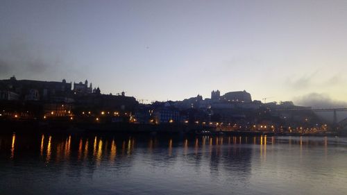River by illuminated buildings against sky at dusk