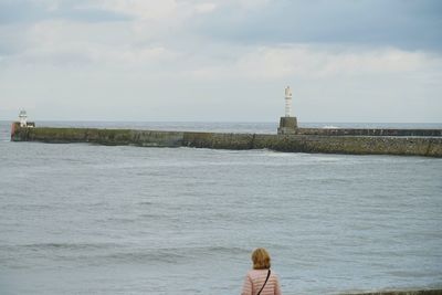 Rear view of woman looking at lighthouse by sea against sky