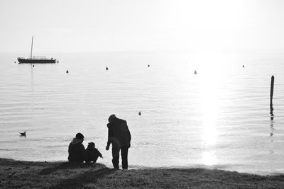 Silhouette people sitting on beach against sky