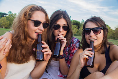 Portrait of young women drinking alcohol while sitting on field