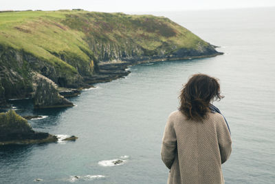 Rear view of woman standing at beach against sky