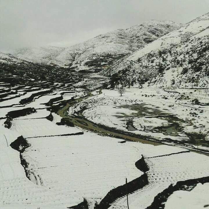 SCENIC VIEW OF SNOW COVERED FIELD BY MOUNTAIN