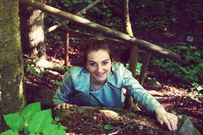 High angle portrait of happy woman standing by rock in forest