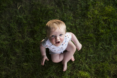 High angle portrait of cute baby boy sitting on grassy field at park