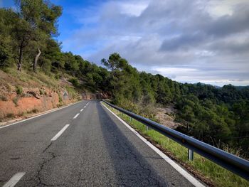 Empty road along trees and against sky