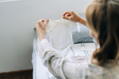 An unrecognizable pregnant woman holds in her hand and looks at an infant bodysuit.
