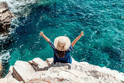 Young woman in summer outfit on cliff above sea.