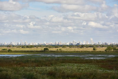 Scenic view of field and cityscape against sky