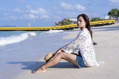 Worried woman sitting on beach with a straw hat on her knees beach by  sea in sunny day time. 