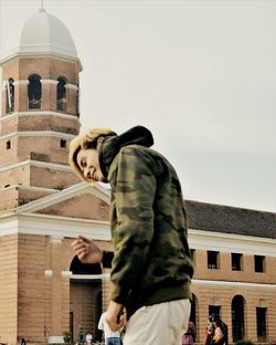 Man standing by building against sky
