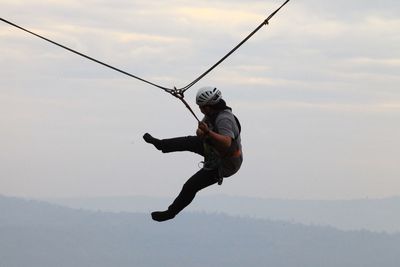 Full length of men ziplining against sky