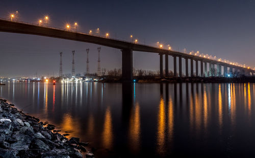 Illuminated bridge over river against sky at night