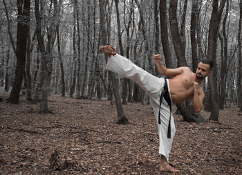 Full length of shirtless man standing in forest