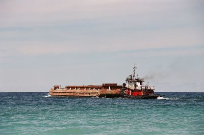 Tugboat pushing barge on sea against sky