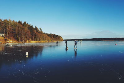 People ice-skating on frozen lake against clear blue sky