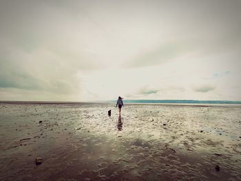 Rear view of woman walking on beach with dog against sky