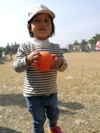 Portrait of cute girl holding ball while standing on field at public park