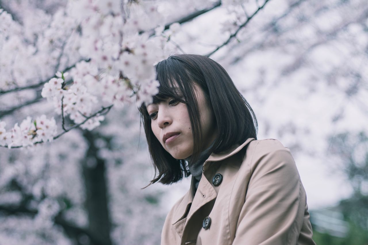 plant, one person, flower, tree, flowering plant, young adult, real people, lifestyles, leisure activity, growth, focus on foreground, nature, casual clothing, fragility, springtime, beauty in nature, freshness, headshot, young women, hairstyle, hair, cherry blossom, outdoors, contemplation, cherry tree