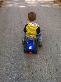 Rear view of boy playing with toy scooter on road