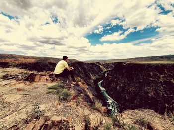 Rear view of person on rock in mountains against sky