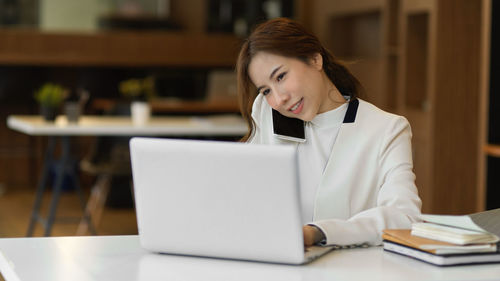 Young woman using phone while sitting on table