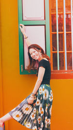 Portrait of smiling young woman standing against yellow door