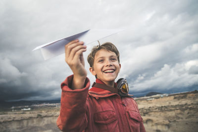 Portrait of smiling boy holding camera against sky