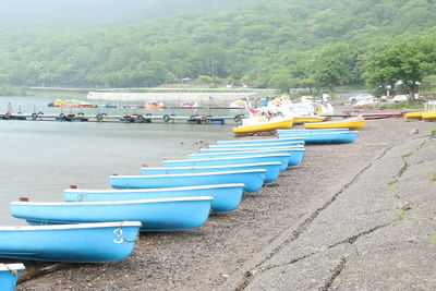 Boats moored on river by trees against sky