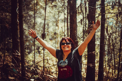 Portrait of young woman standing by tree trunk in forest