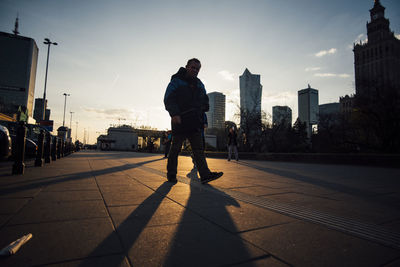 Man standing on street in city against sky during sunset