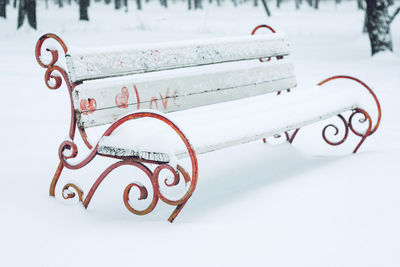 Snow-covered bench in the city amusement park. forged metal and wooden park bench