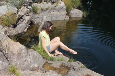 Full length of woman sitting on rock by lake