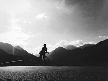 Silhouette man riding bicycle on mountain against sky