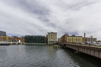 Buildings by river against sky in city