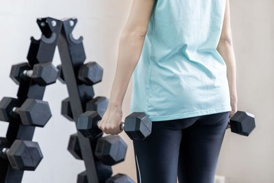 Midsection of woman holding dumbbells at gym