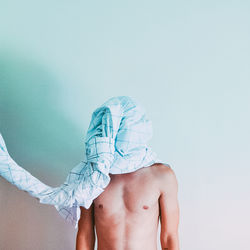 Shirtless man face covered with fabric against white wall