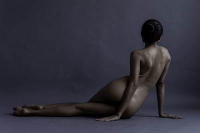 Full length of naked woman sitting against gray background