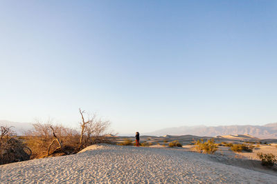 Person standing on sand in desert against clear blue sky